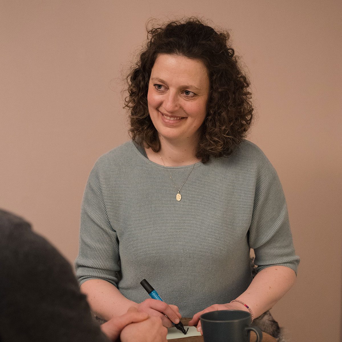 Systematisches Arbeiten mit Hannah Dageförde Lächelnde Therapeutin mit Locken, die Notizen macht und einen Stift hält.